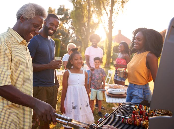 A large family outside enjoying a barbecue, with grandpa at the grill